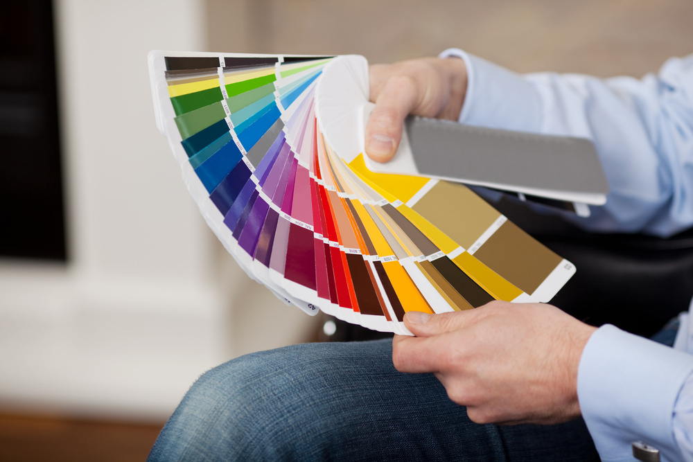 Man holding a set of paint color swatches in all the colors of the spectrum splayed out in his hand as he tries to decide on a new color for his house